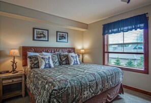 A bedroom with a large bed, two bedside lamps, a nightstand, a window with blinds, and two framed pictures on the wall. - Ski in/ Ski out! Rimfire 351/352 Spacious and Cozy 2 (Snowshoe)