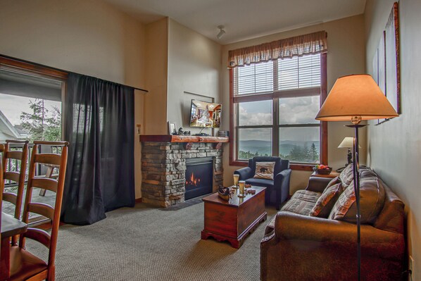 A cozy living room with a fireplace, a sofa, a coffee table, and a TV. - Ski in/ Ski out! Rimfire 351/352 Spacious and Cozy 2 (Snowshoe)