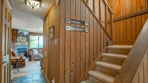A wooden interior with a staircase, a fireplace, and directional signs for 'Cupp Run' and 'Shay's Revenge'. - Tree Top 19, Snowpeak 2 Bedroom Spectacular Townhome Slope Side (Snowshoe)