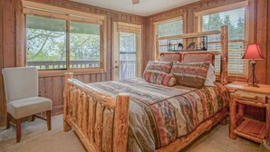 A bedroom with a wooden bed frame, a chair, a nightstand with a lamp, and large windows. - Tree Top 19, Snowpeak 2 Bedroom Spectacular Townhome Slope Side (Snowshoe)