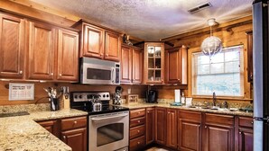 A kitchen with wooden cabinets, granite countertops, stainless steel appliances, and a window with blinds.