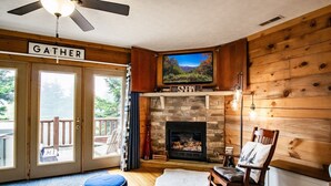 A cozy living room with a fireplace, a television mounted above it, and a sign that reads "GATHER".