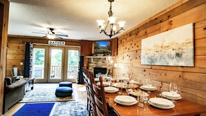 A dining area with a wooden table set for a meal, a chandelier, and a fireplace.