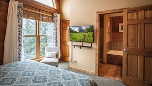 A cozy bedroom with a bed, a television mounted on the wall, and a window with curtains.