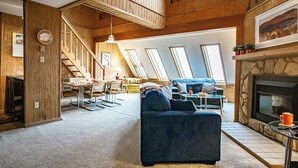 Un vaste espace de vie de style loft, doté d’un haut plafond, de poutres apparentes et d’une cheminée. On y trouve un coin repas avec une table et des chaises, ainsi qu’un coin salon confortable avec un canapé et des fauteuils.