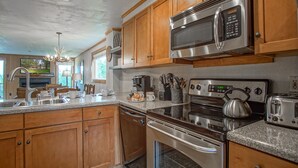 A modern kitchen with wooden cabinets, stainless steel appliances, a granite countertop, and a built-in oven. - Powderidge 40: Slope Side, Sleeps 9 Full Kitchen (Snowshoe)
