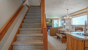 A staircase with wooden railings leading to a living area with a fireplace, dining table, and kitchen counter. - Powderidge 40: Slope Side, Sleeps 9 Full Kitchen (Snowshoe)