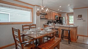 A kitchen with wooden cabinets, a central island with a sink, and a dining area with a wooden table and chairs. - Powderidge 40: Slope Side, Sleeps 9 Full Kitchen (Snowshoe)