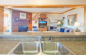 A kitchen with two sinks, a wooden wall, a television, and a sofa with blue cushions.