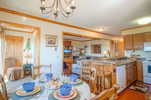 A spacious kitchen with wooden cabinets, a dining area with a table set for four, and a cozy living room with a sofa and a Christmas tree.