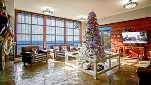 Ein geräumiges Wohnzimmer mit einem großen Weihnachtsbaum, Ledersesseln, einem Fernseher und einem Kamin.