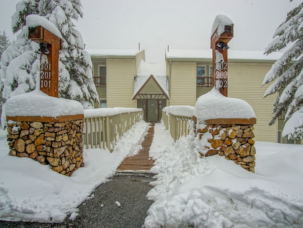 A snow-covered pathway leading to a building with stone pillars and wooden railings.