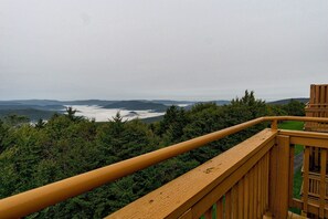 Une terrasse en bois offrant une vue sur une vallée boisée et sur des montagnes lointaines.