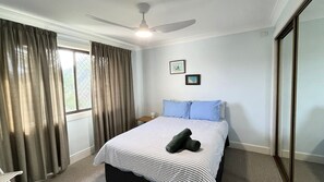 Une chambre d’hôtel avec un lit, un ventilateur de plafond, une fenêtre avec des rideaux et un tableau accroché au mur.