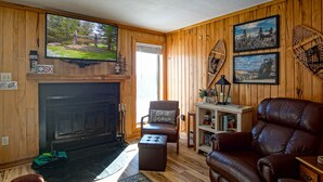 A cozy living room with a fireplace, leather furniture, and wooden walls.