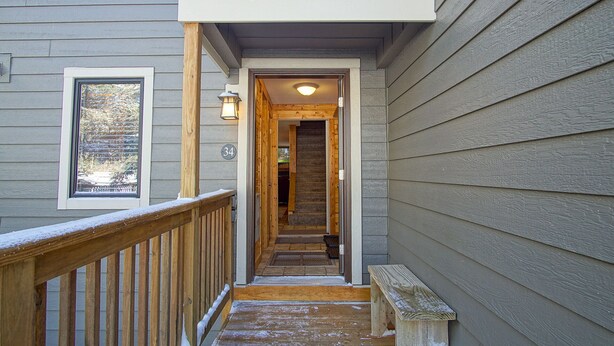 A wooden exterior staircase leading to a door, with a bench at the bottom and a window on the left.