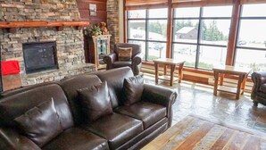 A cozy living room with a stone fireplace, leather sofa, and large windows offering a view of the outside.