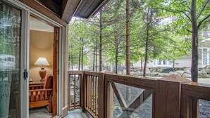 A wooden balcony with a glass door leading to a room with a lamp and a chair.