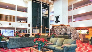 A spacious lobby with a high ceiling, multiple seating areas, a large television, and a stone wall with a mounted animal head.