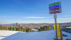 A signpost with directions to various ski slopes and a view of a snowy landscape with trees and a distant lake.