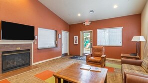 A living room with a fireplace, a television mounted above it, a brown leather chair, a wooden coffee table, and a sofa. - Pinetop | Couples Mountain Retreat | Pool + Hot Tub (Pinetop)
