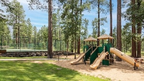 A playground with slides and a shelter, surrounded by trees.