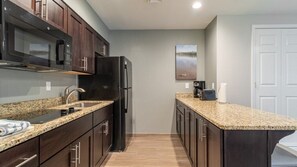 A compact kitchen with dark wood cabinets, a granite countertop, a black refrigerator, and a microwave. - Pinetop | Couples Mountain Retreat | Pool + Hot Tub (Pinetop)