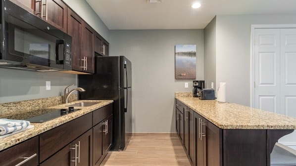 A compact kitchen with dark wood cabinets, a granite countertop, a black refrigerator, and a microwave.