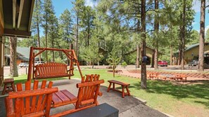 A wooden deck with benches and a swing set, surrounded by trees and a building with a covered area. - Pinetop | Couples Mountain Retreat | Pool + Hot Tub (Pinetop)