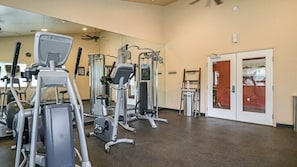 A gym with various exercise machines, a large mirror, and a door with a red frame.