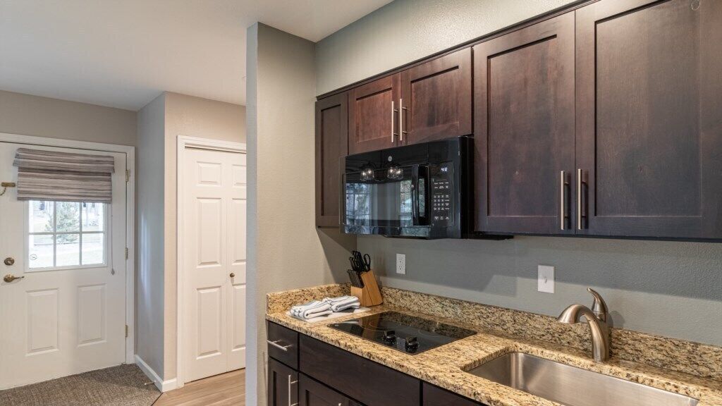A kitchen with dark wooden cabinets, a stainless steel sink, and a black microwave.