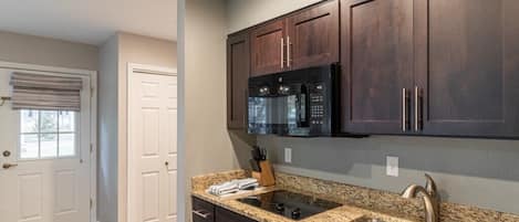 A kitchen with dark wooden cabinets, a stainless steel sink, and a black microwave.