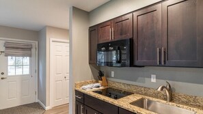 A kitchen with dark wooden cabinets, a stainless steel sink, and a black microwave.