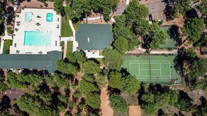 Luchtbeeld van een pand met een groot zwembad, tennisbanen en omliggend groen.