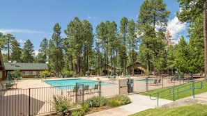 A pool area with lounge chairs and a fenced deck, surrounded by tall trees.