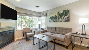 Een woonkamer met een open haard, een bank, een salontafel, een televisie en kunstwerken aan de muur.