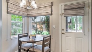 A dining area with a round table and chairs, a chandelier, and windows with blinds.