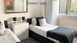 Une chambre d’hôtel avec un lit, une table de chevet, une commode, un miroir et une fenêtre avec des stores.