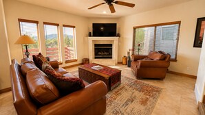 A living room with leather sofas, a fireplace, a television, and large windows. - 4BD Home  Private Hot Tub  Minutes to Slopes & Main St (Park City)