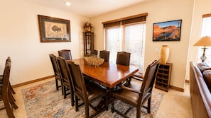 A dining room with a wooden table, six chairs, a vase, and two wall-mounted paintings.