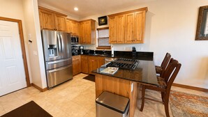 A kitchen with wooden cabinets, stainless steel appliances, a black countertop, and a dining area with wooden chairs. - 4BD Home  Private Hot Tub  Minutes to Slopes & Main St (Park City)