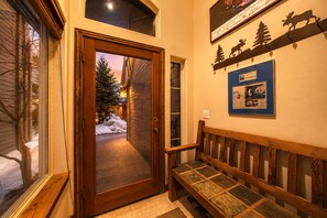 A wooden door leading to a snowy outdoor area, a bench, and a wall with a sign and a framed picture. - 4BD Home | Private Hot Tub | Minutes to Slopes & Main St (Park City)