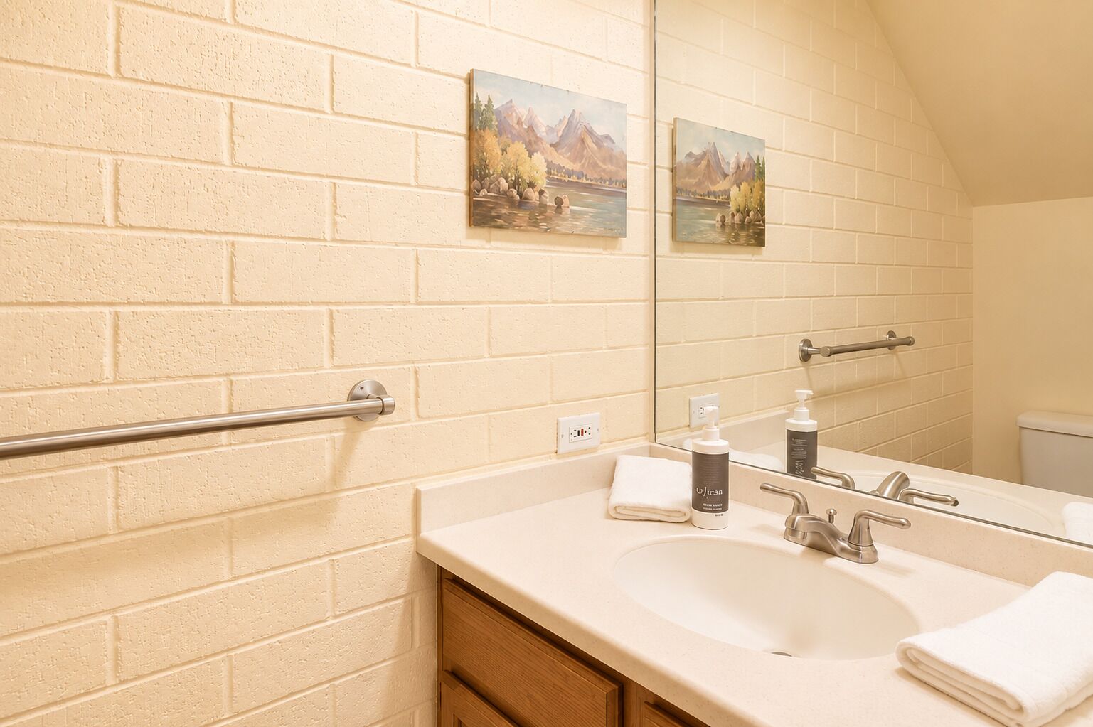 Une salle de bain avec un lavabo blanc, un miroir, une serviette et un tableau représentant un paysage de montagne.