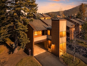 Ein modernes, mehrgeschossiges Haus mit integrierter Garage, umgeben von Bäumen und einer hügeligen Landschaft.