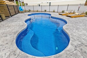 Une piscine au design incurvé, entourée d’une clôture en métal noir et d’une terrasse carrelée.