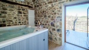 A stone-walled room with a wooden floor, a large bathtub, and a bottle of champagne. - Stunning private villa for 4 people with hot tub, WIFI, A/C, TV, terrace and panoramic view (Seggiano)