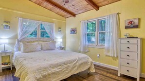 Une chambre à coucher comprenant un lit, des tables de chevet, une commode et deux fenêtres avec des rideaux.