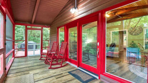 Une véranda avec des portes vitrées à cadre rouge, un plancher en bois et des fauteuils à bascule.