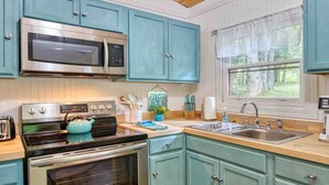 Une cuisine avec des armoires de couleur turquoise, un four à micro-ondes en acier inoxydable, une cuisinière noire et un évier placé sous une fenêtre.