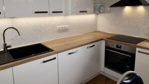Una cocina moderna con armarios blancos, encimera de madera, pileta negra, estufa y extractor de aire negro.